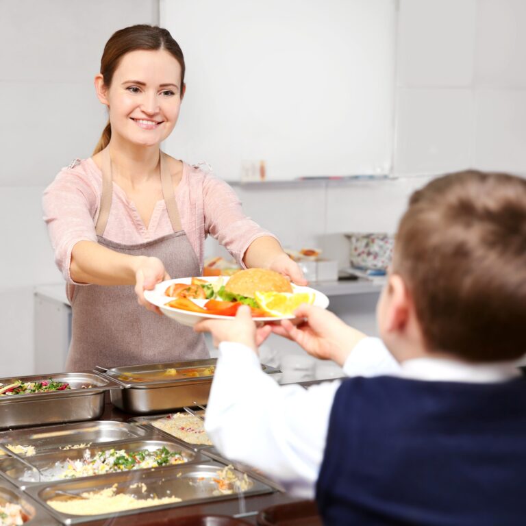 woman giving lunch to school boy in cafeteria