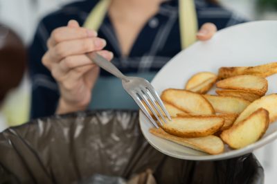 Cholesterol of junk meal is fat meal, asian young household woman scraping, throwing food leftovers into the garbage, trash bin from potato chip, snack in kitchen. Environmentally responsible, ecology